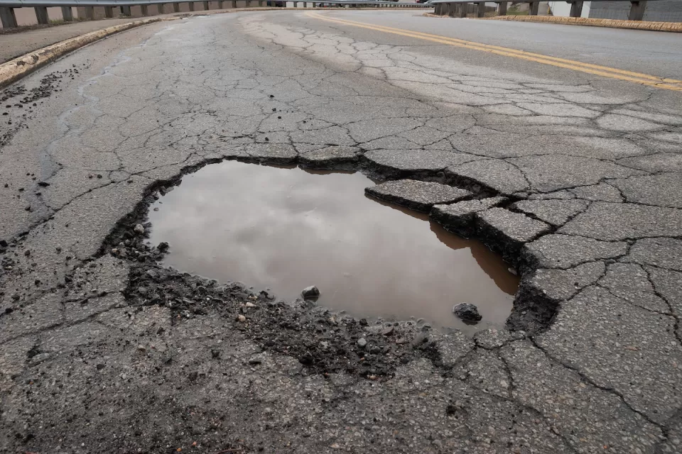 CLose-up of pothole in asphalt road filled with water reflecting grey cloudy sky.